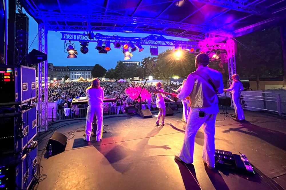 Aufnahme des Fürth Festivals aus der Perspektive der Künstler. Im Vordergrund spielende Musiker aus der Bühne, im Hintergrund das Publikum 