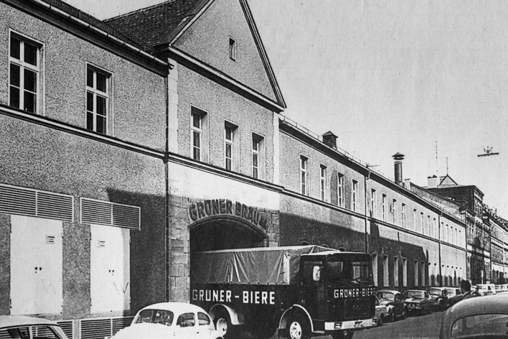 Eine alte Schwarz-Weiß-Aufnahme des Grüner Bräu Gebäudes. Durch die Ausfahrt kommt ein alter Laster von Grüner Biere.